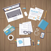 Office work place with documents, laptop, notebook, wallet, phone, watch, glasses, pencil, pen,  graphs and charts, headphones, coffee, forms. Wooden desk with supplies. Organization, management.