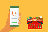istock Online Grocery Shopping And Delivery Concept With Shopping Basket Full Of Vegetables And Human Hand Holding Mobile Phone. 1350583682