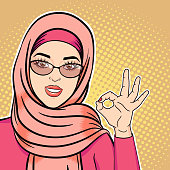 Pop art happy arab woman in hijab smiling and showing ok sign, vector illustration of successful muslim woman in retro comic style