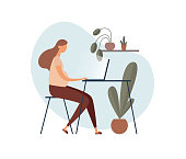 Pregnant woman in casual clothes sitting at table and using laptop while working on remote project in cozy home office decorated with potted plants