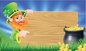 Cartoon Saint Patricks day leprechaun pointing at a sign wood sign with shamrock in his hat and a pot of gold