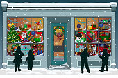 Storefront Christmas window filled with vintage toys, presents and colorful decorations. Silhouettes of children are outside, looking into the windows while snowflakes fall to the snowy sidewalk.