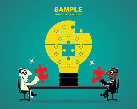 Two businessmen sitting at the conference table and completing the jigsaw of idea light bulb