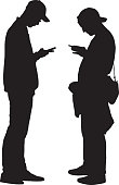 Vector silhouette of two young men looking at there smart phones.