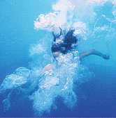 Underwater view of Asian girl jumping into pool surrounded with exploding bubbles.