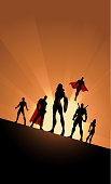 A silhouette style illustration of a team of superheroes with female leader with sunlight in the background and wide space for your copy.