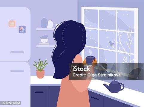 istock Woman with cup of tea or coffee in hands standing in kitchen at home and looking out window 1285914663