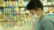 istock Asian boy wearing face mask reading cartoon book in Bookstore with family, social distancing lifestyle concept. 1306266210
