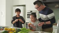 istock asian chinese father and daughter cutting oranges and eating together with son in kitchen counter 1337451809