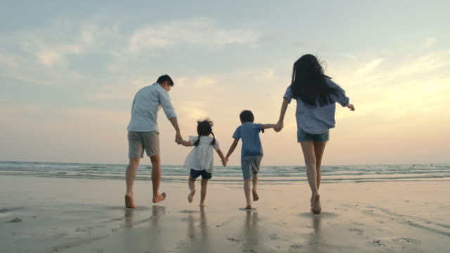 SLOW MOTION - Asian family running on the beach at sunset with happy emotion. Family, Holiday and Travel concept. Back Rear View.