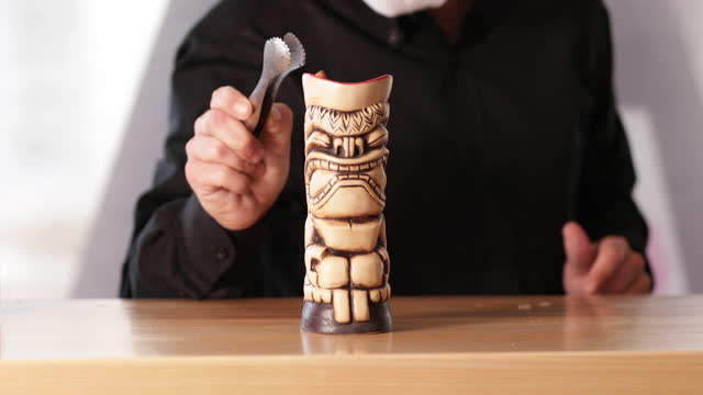 Barman Adds A Cinnamon Stick To Cocktail Drink Served In A Wooden Tiki At The Bar Counter