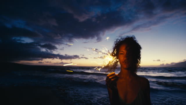 Beautiful young woman walking with sparkler fireworks on the beach at twilight