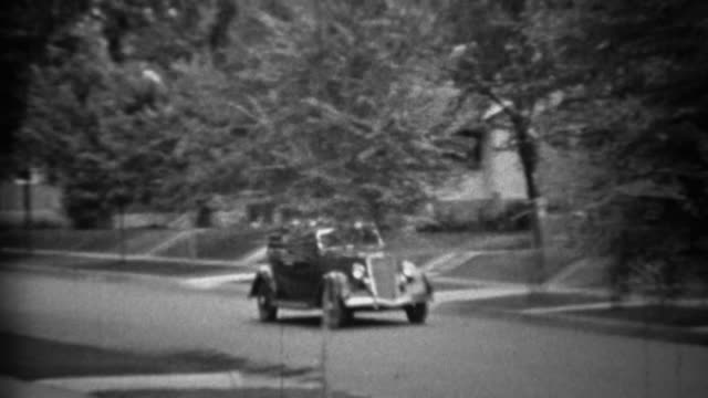 1935: Classic new black Plymouth car driving residential neighborhood.