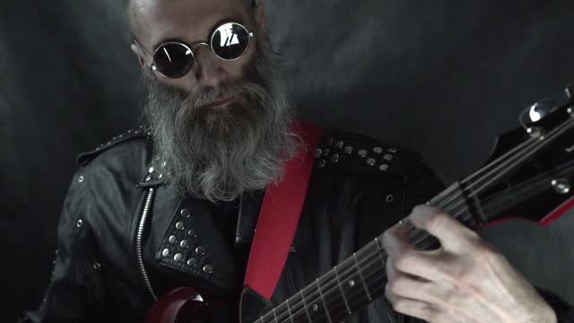 Close up of bearded rock musician head with shaved temples wearing round glasses and leather jacket