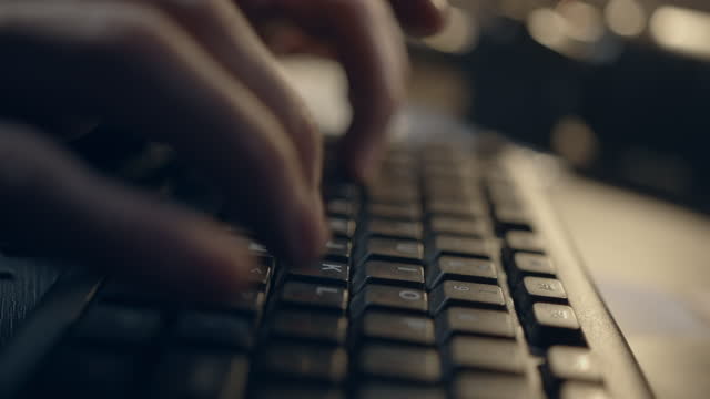 Close-up of a man's fingertips tapping rapidly on a keys on a computer keyboard