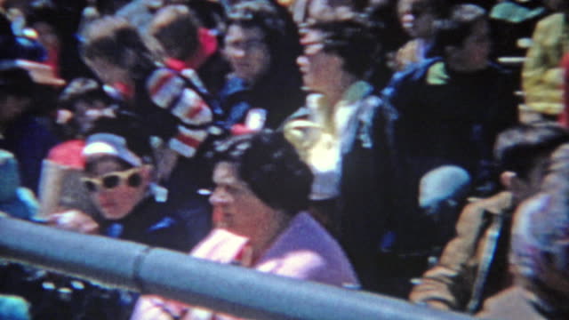 1963: Crowd seated watching high school track meet during bright summer day.