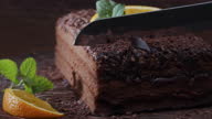 istock Cutting a slice of chocolate cake decorated with fresh orange and mint. Extreme close-up 1276775644
