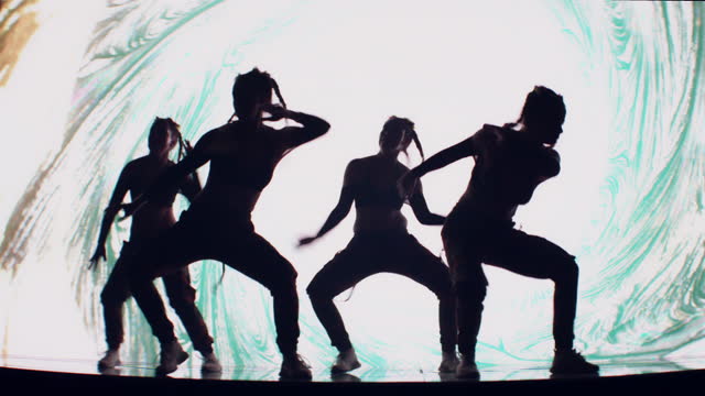 Dancers silhouettes performing on stage with projection background. Inside surreal, digital landscape with neon lightning