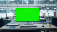 istock Desktop Computer Monitor with Mock Up Green Screen Chroma Key Display Standing on the Desk in the Modern Business Office. In the Background Glass Wall with Big City Office. Zoom Out Shot. 1354060823