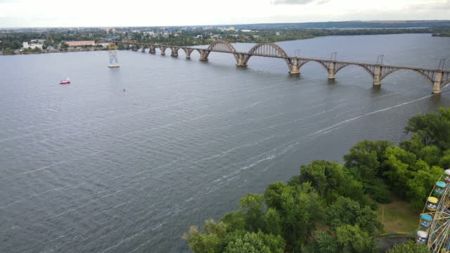 Europe's unique arched railway bridge over the Dnieper River with a lively embankment and yacht club under it Aerial view of the old arched railway Merefo-Kherson bridge in the city of Dnipro.