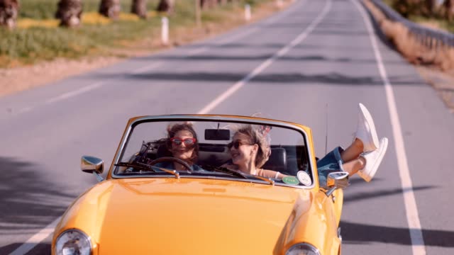 Happy women on road trip driving vintage yellow cabriolet car