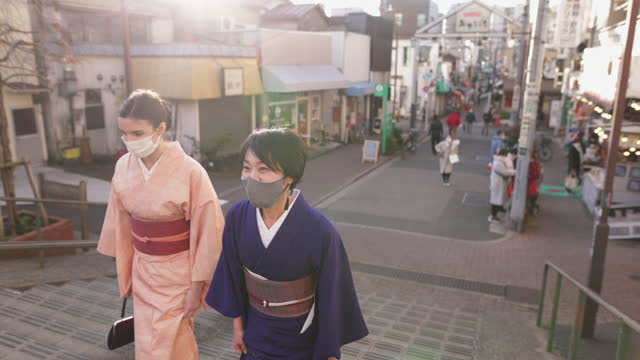 Japanese and Caucasian women in kimono with protective face mask walking up stairs at sunset time