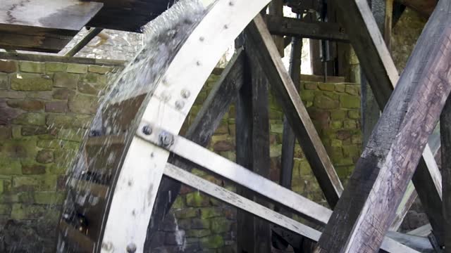 Large colonial American water wheel turns as water pours in