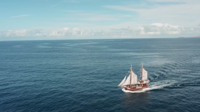 A lonely old pirate ship with white sails glides over the waves on the open sea in clear weather with a favorable wind