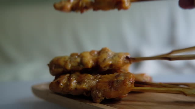 Man hand put Thai style chicken grilled skewers on wood tray, delicious cuisine. Street Thai food