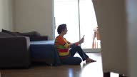 istock Mature woman sitting on the floor using smartphone at home 1332394243