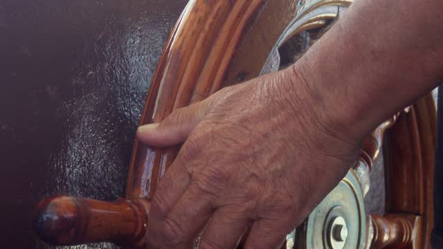 Men's hands hold the rudder of the ship