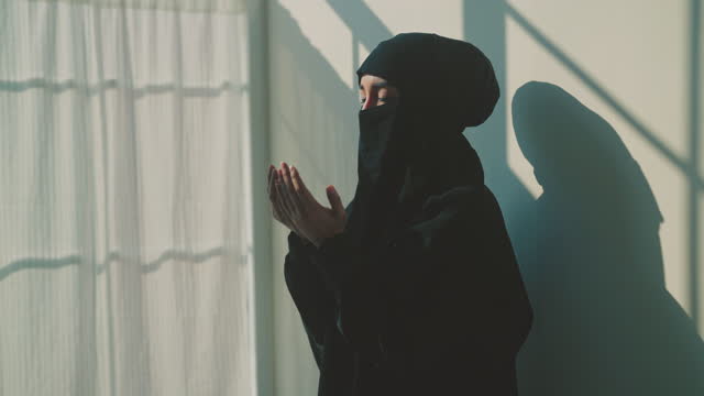 Muslim woman praying to allah with a reflection on the wall of the room.