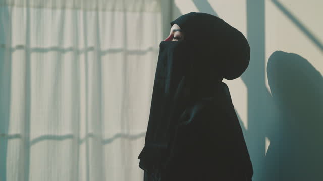 Muslim woman praying to allah with a reflection on the wall of the room.