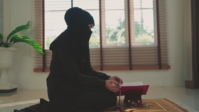 Muslim woman wear black dress holding his prayer beads while sitting in living room at home.