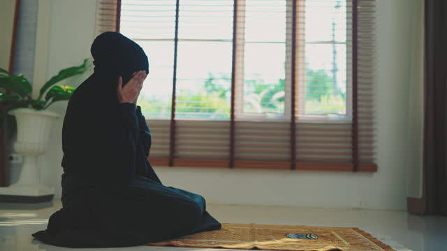 Muslim woman wear black dress praying to allah in living room at home.