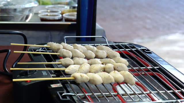 Thai style Hand of street vendors hand is cooking of meatball pork balls grill on charcoal stove at street food market Thailand. Traditional thailand food style.