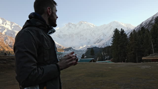 The man drinking a hot tea at the scenic mountains background