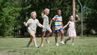 istock Tracking side view shot of group of happy multiethnic kids running on green grass holding hands. Diverse children hopping on lawn in park or woodland in slow motion and screaming with excitement 1329395682