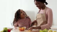 istock Young african american mother preparing vegetable salad, curly little daughter coming and eating fresh pepper at kitchen 1322988259