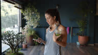 istock Young Latin American woman drinking a green juice at the gym while checking messages on smartphone with headphones around her neck 1306765355