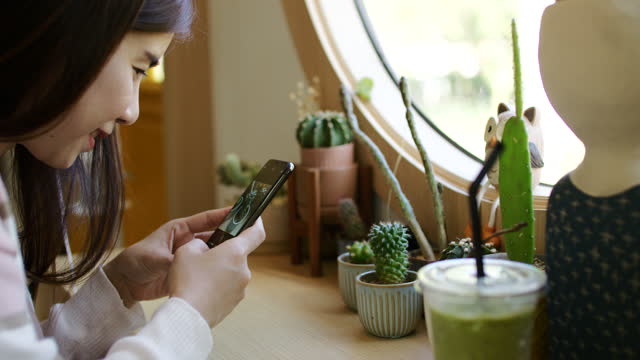 Young woman using phone trying to snap cactus